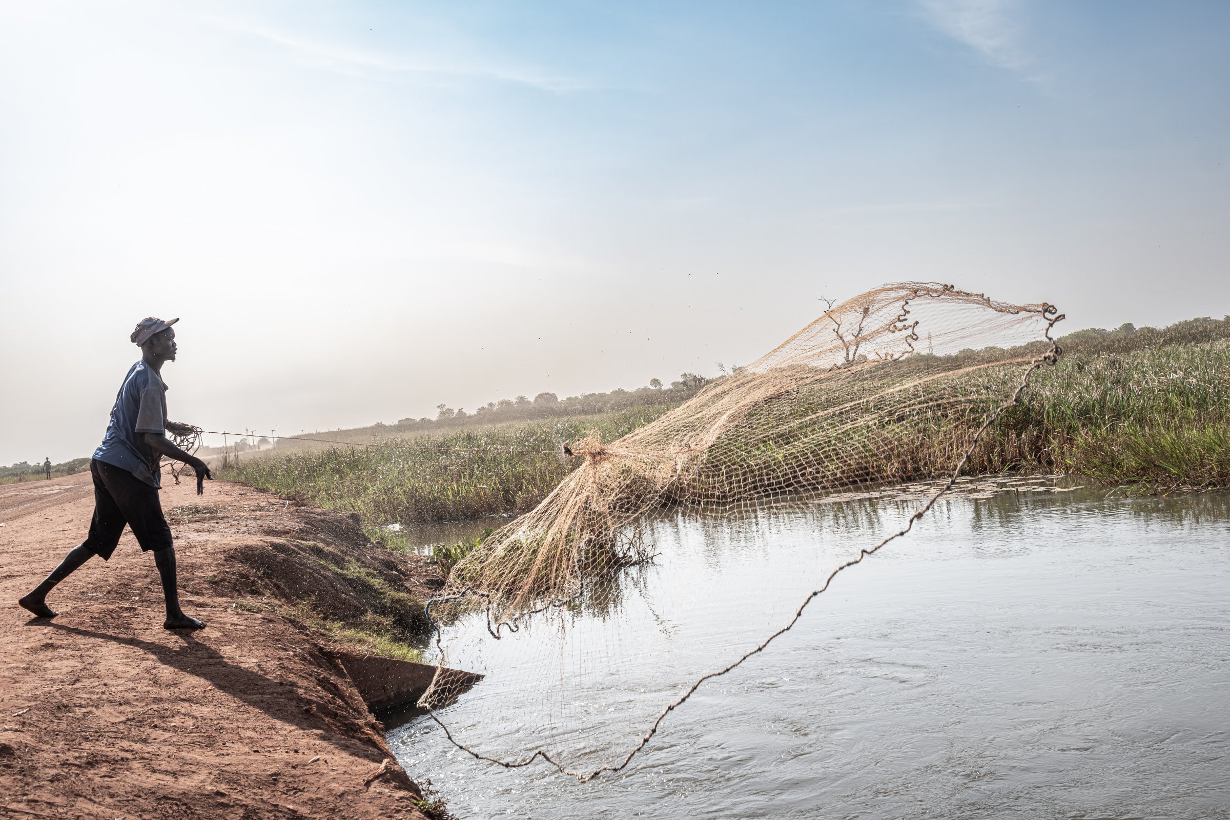 Un pêcheur déplacé lance son filet depuis une digue de Rubkona. Faute de terres cultivables et de troupeaux, de nombreuses familles se sont tournées vers la pêche pour survivre. État d'Unité, Soudan du Sud, mars 2026.