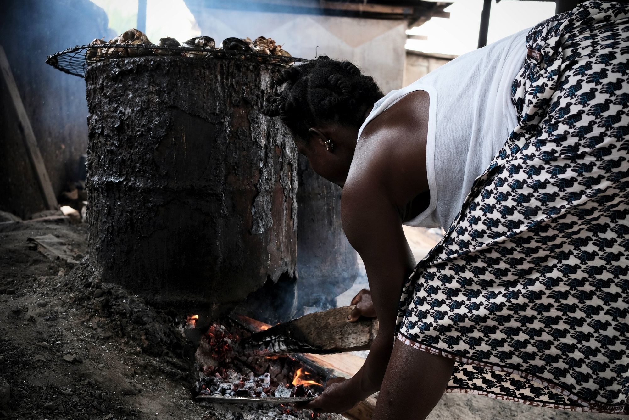Véronique fume le poisson au moyen de barils. Abobo Doumé, Abidjan, 2024.