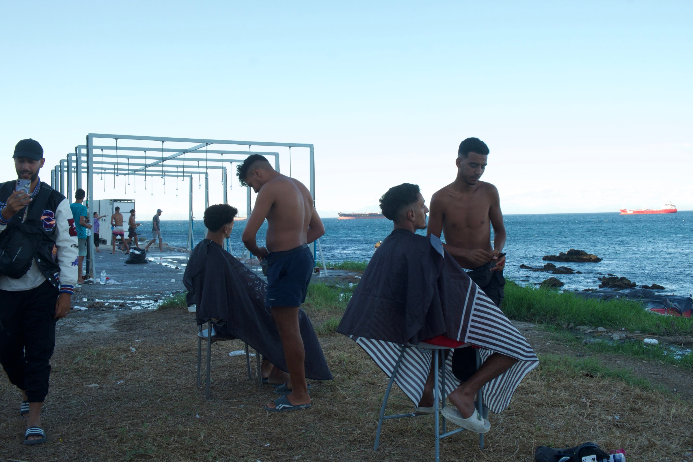Des jeunes exilés se coupent les cheveux à proximité du campement informel installé en bord de mer, à la Plage du Trampolín.