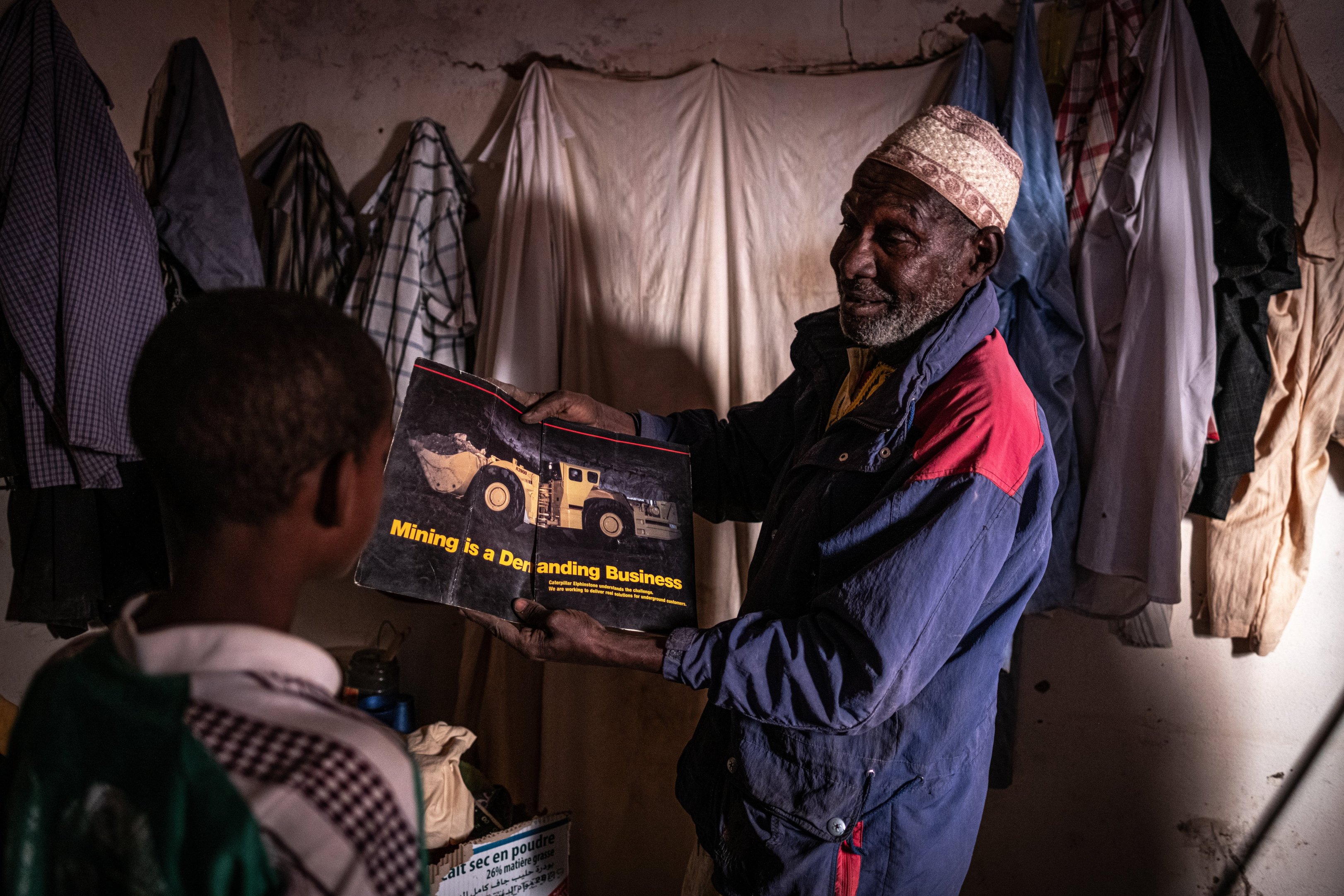À l'intérieur de sa maison, à Akokan, Boukari Mahaman, un ancien travailleur de la Cominak, montre à l'un de ses fils la photo d'une grande machine minière semblable à celles qu'il utilisait lorsqu'il travaillait dans les mines d'uranium.