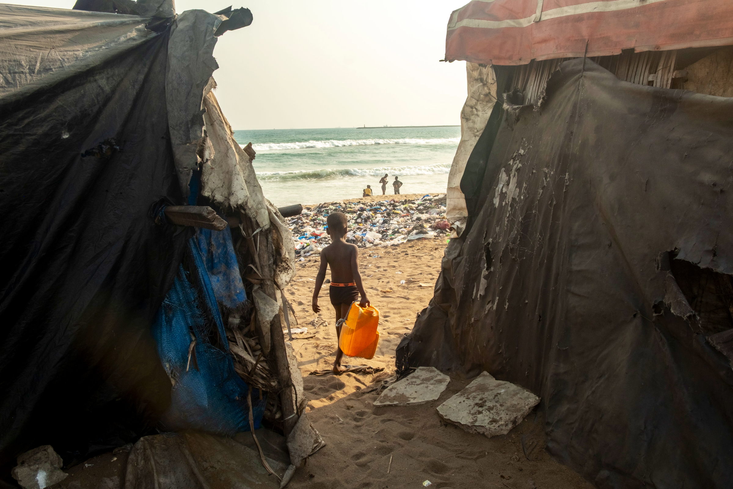 Un enfant prélève de l'eau de mer pour les usages domestiques, devant une montagne de déchets laissés depuis deux ans (2025).