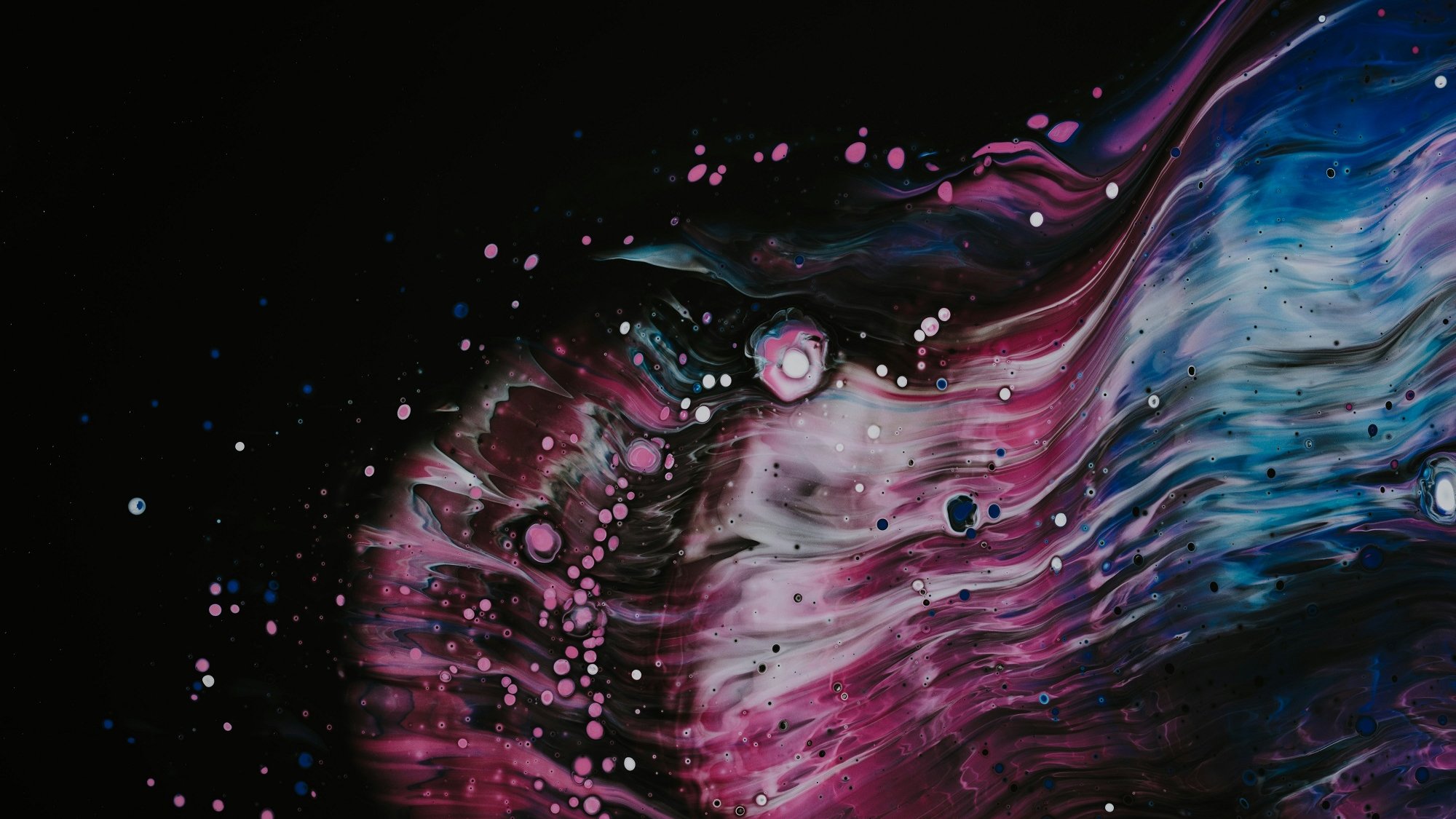 L'image présente une explosion de couleurs vibrantes sur un fond noir, évoquant un cosmos mystérieux. Des ondulations fluides rappellent des vagues, avec des nuances de bleu, de rose et de violet se mêlant harmonieusement. Des éclats de blanc, semblables à des étoiles dispersées, ajoutent une dimension de profondeur et de texture, créant une atmosphère dynamique et captivante. L'ensemble évoque un mouvement constant, presque euphorique, incitant à l'évasion et à la contemplation.