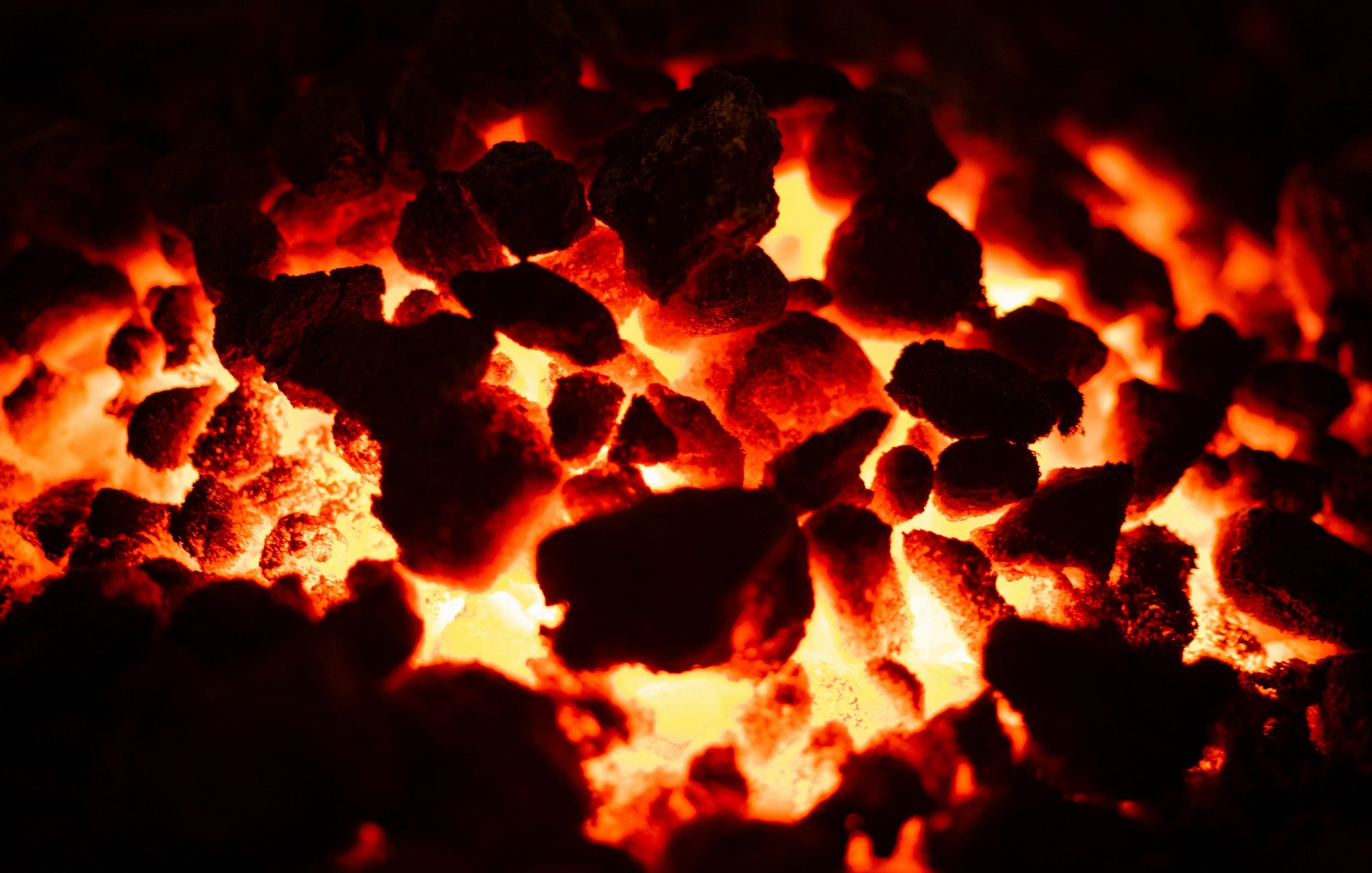 L'image montre une vue rapprochée d'un lit de braises ardentes. On peut imaginer une surface irrégulière composée de petites pierres et de morceaux de charbon, dont la couleur varie du noir au rouge incandescent. Certaines zones sont illuminées d'une lueur vive, créant un contraste saisissant avec l'obscurité environnante. Cette chaleur intense peut presque être ressentie, évoquant l'idée d'un feu puissant et vivant. L'atmosphère générale est à la fois captivante et intimidante, rappelant la force de la nature.