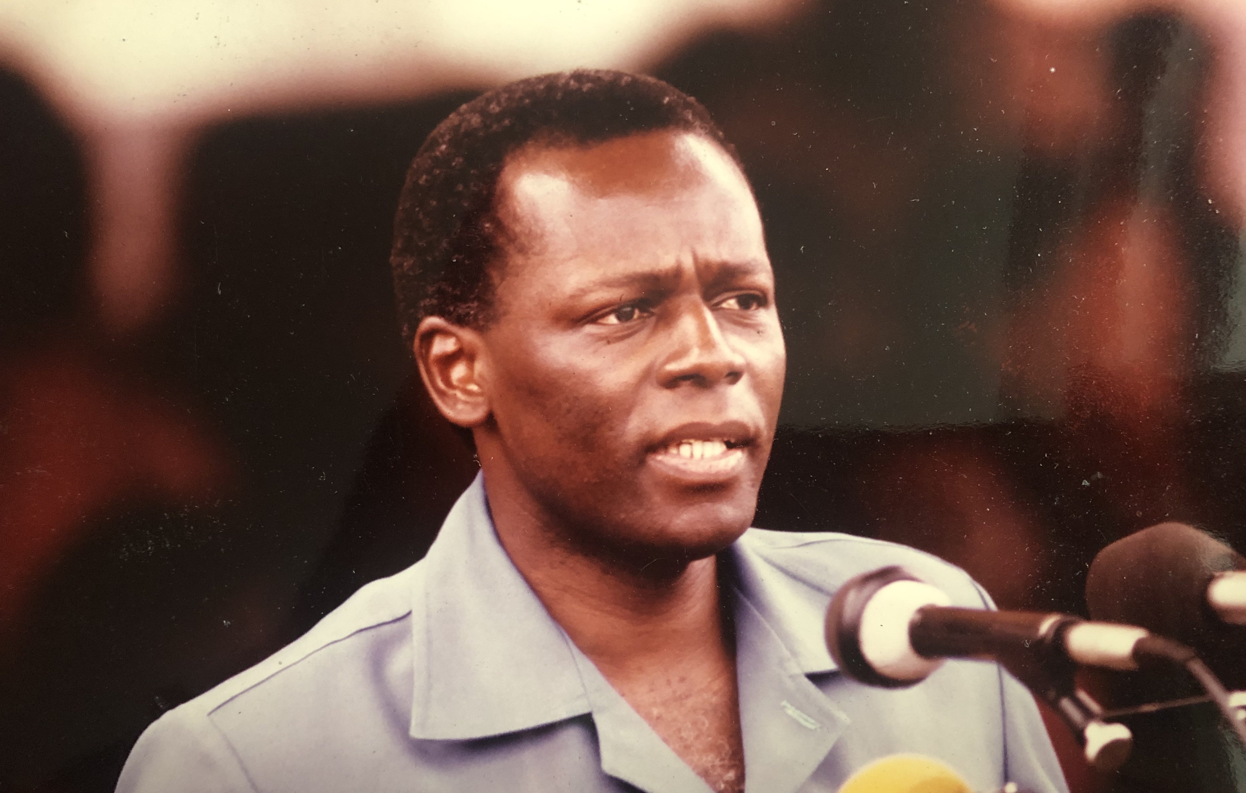 L'image montre un homme en train de prononcer un discours devant un microphone. Il porte une chemise de couleur bleue et semble sérieux et engagé dans ses propos. Son visage exprime une certaine détermination, et il se tient droit. Il y a plusieurs microphones devant lui, et un public peut être présent en arrière-plan, bien que non visible sur cette image. L'atmosphère donne l'impression d'un moment important lors d'un discours ou d'une déclaration publique.