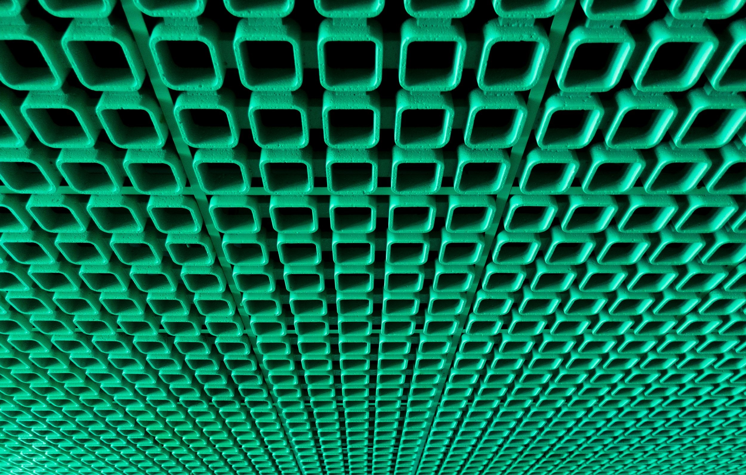 L'image montre un motif répétitif de carrés de couleur verte. Ces carrés sont disposés de manière régulière et forment une sorte de grille ou de treillis. La texture semble lisse, et les angles des carrés sont bien définis. L'ensemble crée une impression de profondeur et de répétition, avec une lumière qui pourrait accentuer les ombres des différents éléments. Cette composition évoque une sensation de structure et d'ordre.