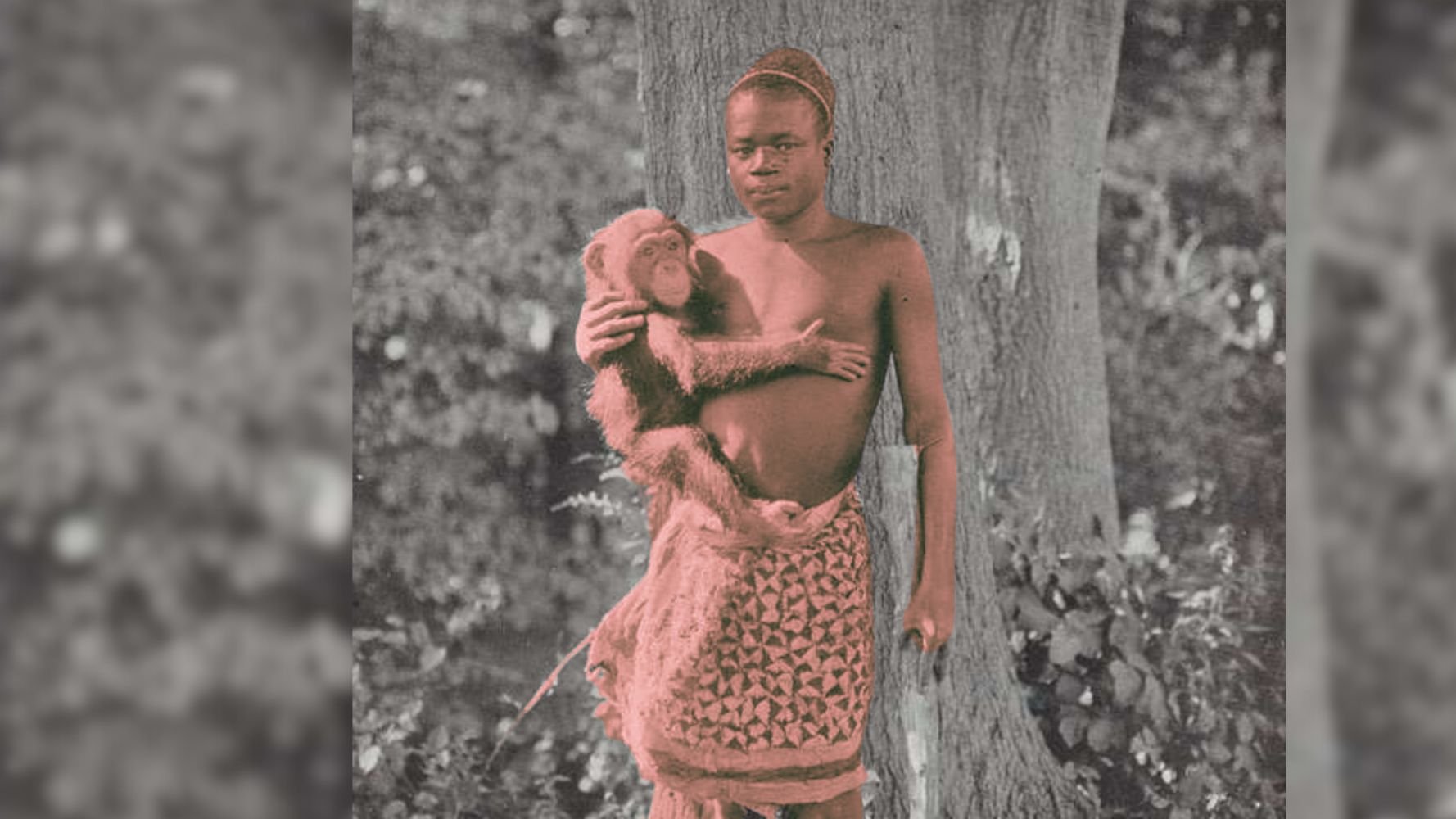 L'image montre un jeune garçon debout près d'un grand arbre. Il porte une jupe tissée, et il a un regard sérieux. Dans ses bras, il tient un petit singe, qui semble curieux et détendu. L'ambiance de la photo est naturelle, avec du feuillage verdoyant en arrière-plan. La scène évoque une connexion entre l'enfant et l'animal, soulignant une relation amicale et intime dans un cadre naturel.