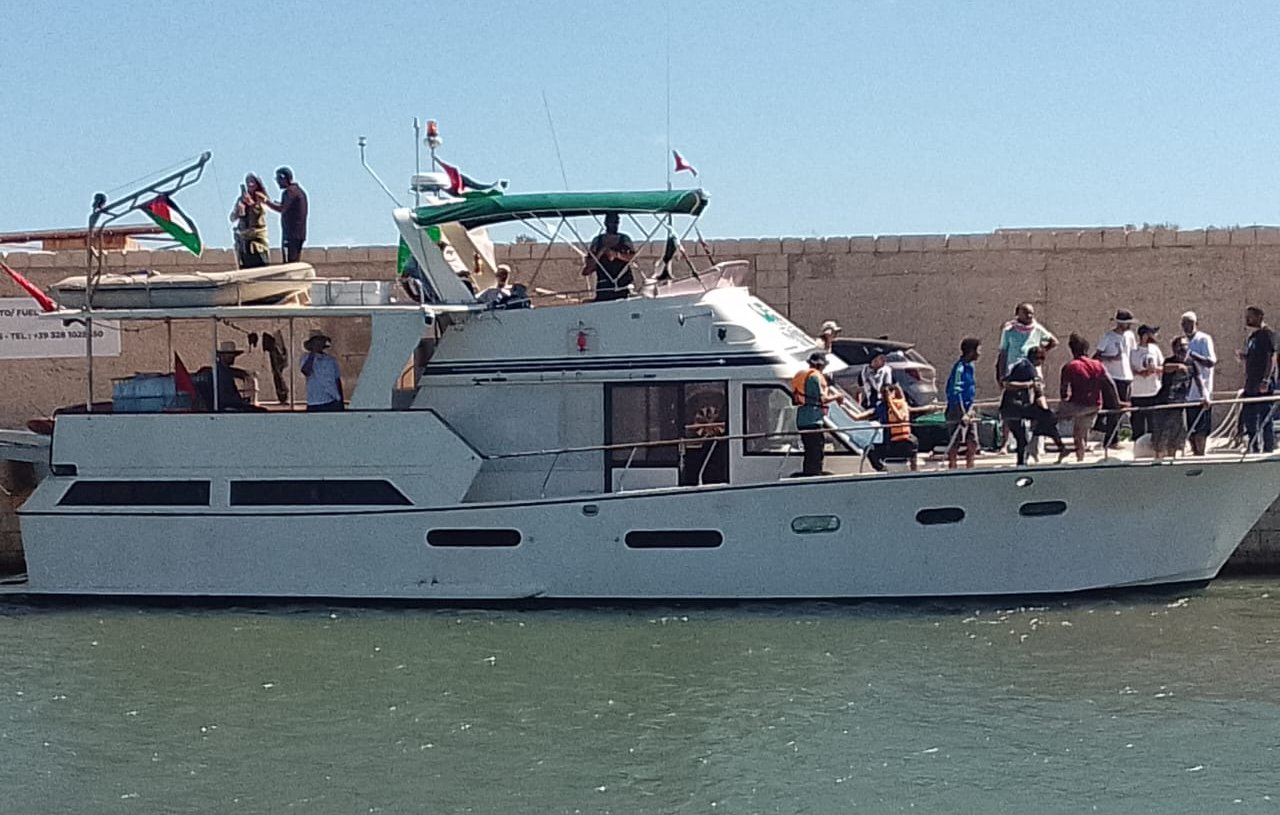 Imaginez un bateau de plaisance élégant, amarré à un quai au bord de l'eau. Sa coque est blanche, et le soleil illumine son pont supérieur qui est équipé d'un auvent vert. Plusieurs personnes se trouvent sur le bateau et sur le quai ; certaines semblent s'apprêter à embarquer, tandis que d'autres discutent joyeusement. L'arrière-plan montre un mur de pierre beige qui contraste avec le bleu de l'eau. L'atmosphère est animée et estivale, évoquant une journée de détente en bord de mer.