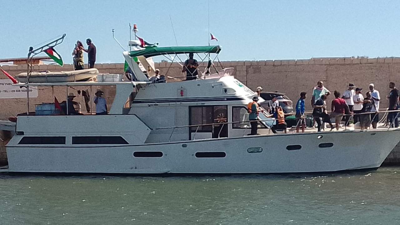Imaginez un bateau de plaisance élégant, amarré à un quai au bord de l'eau. Sa coque est blanche, et le soleil illumine son pont supérieur qui est équipé d'un auvent vert. Plusieurs personnes se trouvent sur le bateau et sur le quai ; certaines semblent s'apprêter à embarquer, tandis que d'autres discutent joyeusement. L'arrière-plan montre un mur de pierre beige qui contraste avec le bleu de l'eau. L'atmosphère est animée et estivale, évoquant une journée de détente en bord de mer.