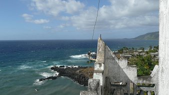 Imaginez-vous au sommet d'une vieille tour, où l'air est frais et légèrement salé. Devant vous s'étend un vaste océan d'un bleu profond, parsemé de vagues qui dansent et s'écrasent sur des rochers sombres. Au loin, vous pouvez percevoir la côtes, avec des palmiers se balançant doucement au gré du vent. Le ciel est parsemé de nuages blancs qui flottent, créant un jeu de lumière sur l'eau. Sur votre droite, des paysages verdoyants de collines se dessinent, ajoutant à la beauté sauvage de cet endroit. C'est un panorama paisible et apaisant, où la nature semble en harmonie avec l'horizon.