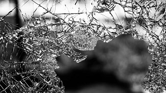 L'image montre un morceau de verre brisé, dont les nombreux éclats forment des motifs irréguliers. On peut ressentir la fragilité et la netteté des bords du verre. La lumière semble traverser certains éclats, créant des jeux d'ombre et de lumière. L'arrière-plan est flou, évoquant une ambiance sombre et mystérieuse. Cette composition souligne la beauté inattendue du verre cassé, tout en évoquant une sensation de vulnérabilité.