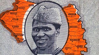 L'image représente une illustration stylisée de la carte de la Guinée, mettant en évidence ses régions en orange. Au centre, un portrait d'un homme portant un chapeau traditionnel est encadré par la carte. Le fond est décoré avec des motifs en noir et blanc, et le mot "Guinée" est inscrit en haut de l'image. Cette composition évoque une célébration de l'identité culturelle et géographique du pays.