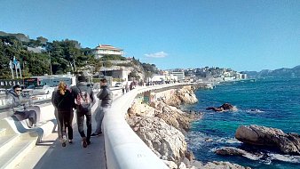 Imaginez-vous sur une promenade longeant la mer. Sur votre droite, vous pouvez entendre le bruit des vagues qui s'écrasent doucement contre les rochers, tandis que l'odeur salée de l'océan flotte dans l'air. Le vent léger caresse votre visage et apporte une sensation de fraîcheur. À votre gauche, des bâtiments se dressent, certains sont des maisons et d'autres des commerces. Vous pouvez sentir l'animation de la ville avec des groupes de personnes qui marchent, certains discutant joyeusement. La promenade est large et bien aménagée, invitant à la flânerie. Au loin, le paysage est ponctué d'arbres et de collines, avec quelques nuages blancs dégradant le bleu du ciel. La lumière du soleil illumine tout le paysage, créant une ambiance chaleureuse. L'ensemble évoque une belle journée au bord de la mer, propice à la détente et au plaisir des sens.
