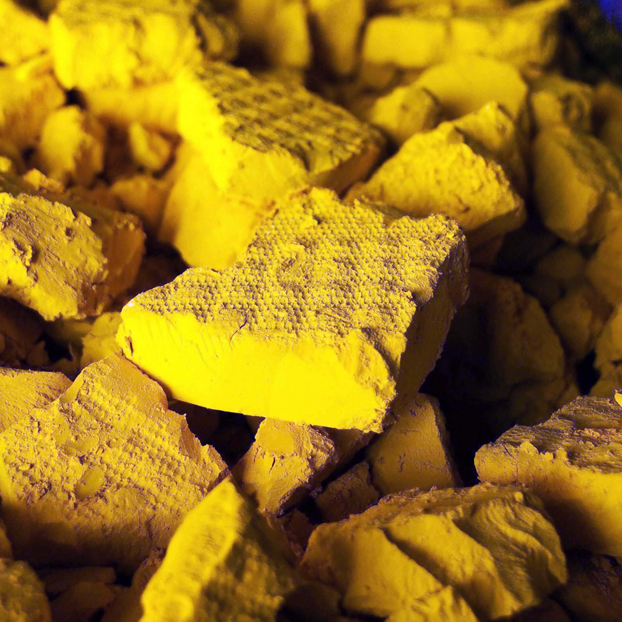 L'image montre un tas de morceaux de matière d'une couleur jaune vif. Les morceaux sont anguleux et irréguliers, présentant des surfaces rugueuses et poudreuses. La lumière semble créer des ombres subtiles, accentuant les textures des éclats. L'ensemble de la composition transmet une impression de dépouillement et de matière brute, évoquant à la fois la richesse de la couleur et une certaine fragilité des formes.