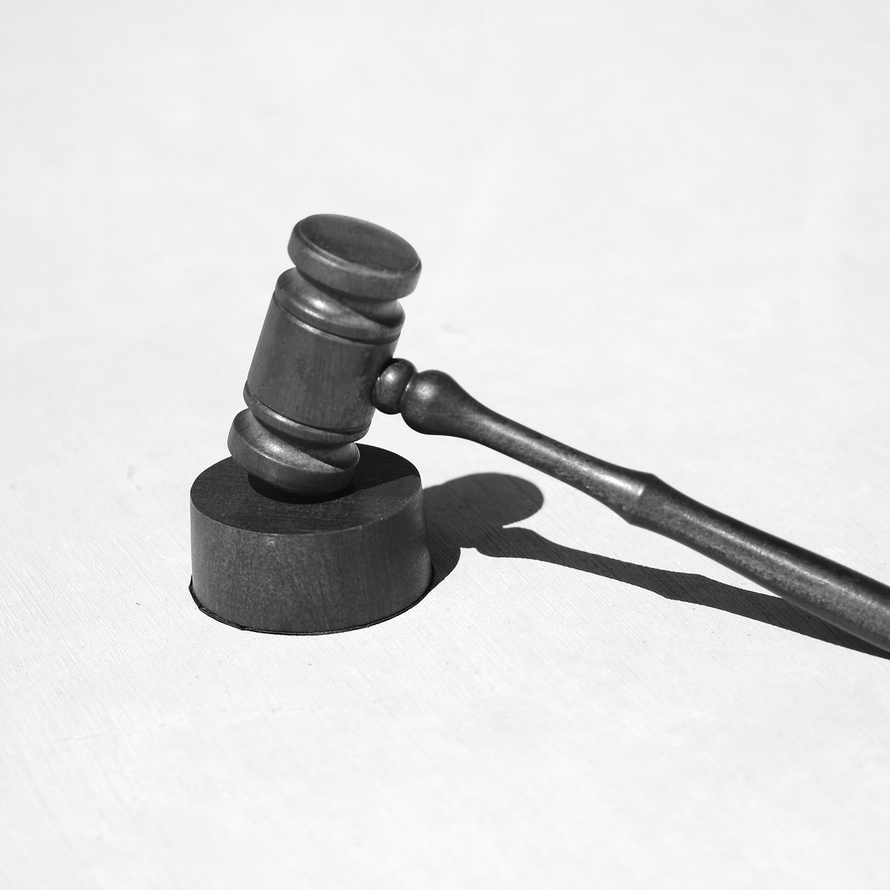 L'image présente un maillet de juge, souvent appelé "gavel". Il est en métal noir, avec une partie cylindrique plus épaisse à sa base et un long manche. Le maillet repose sur une surface claire, ce qui crée un contraste marqué. La lumière éclaire l'objet, projetant une ombre sur le côté. Le maillet est couramment associé au monde de la justice et des tribunaux, symbolisant l'autorité et la prise de décision.
