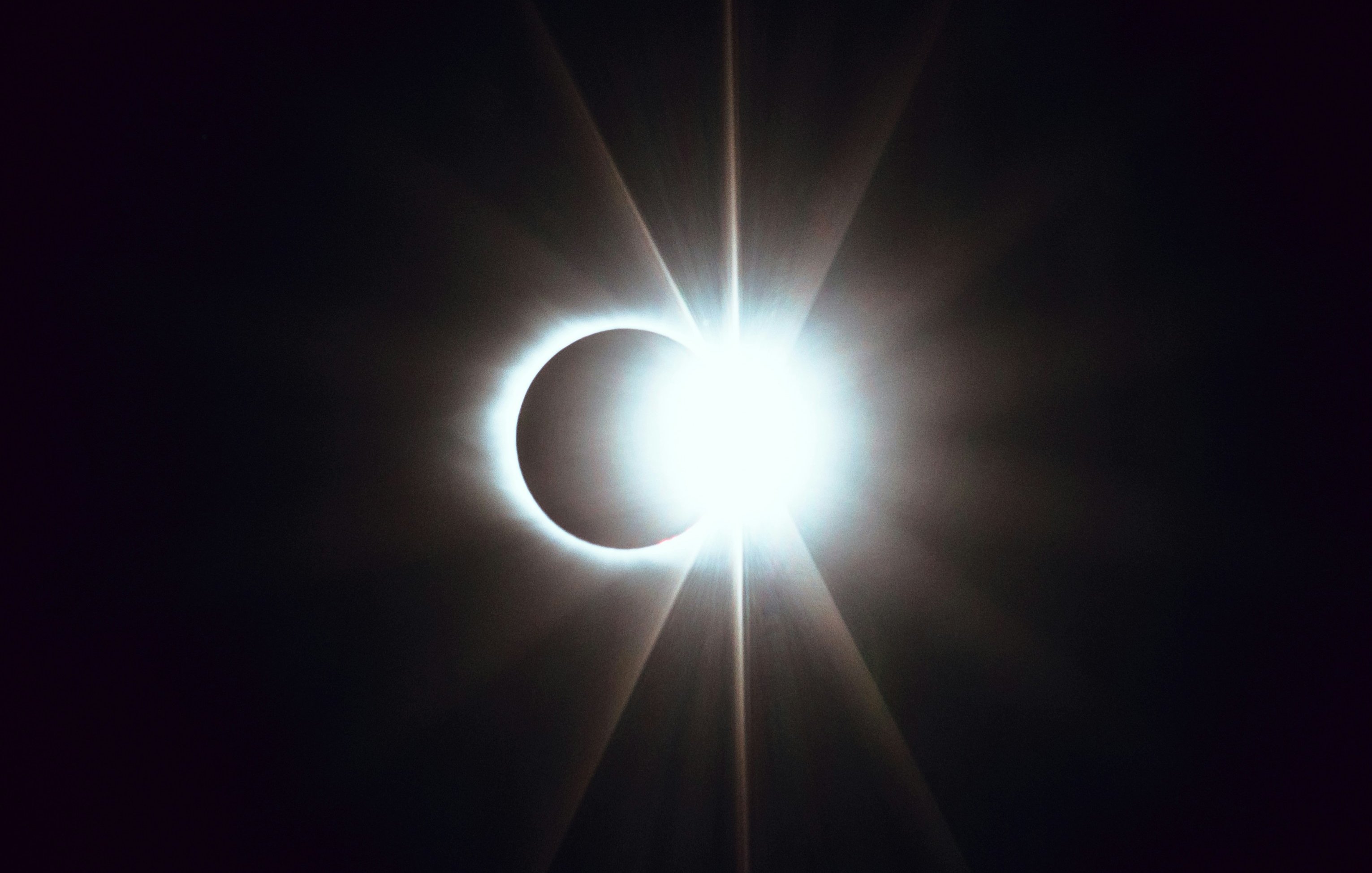 L'image représente un phénomène astronomique spectaculaire : une éclipse solaire. Au centre, un cercle éclatant de lumière intense, représentant le soleil, est partiellement recouvert par la silhouette sombre de la lune. Cette superposition crée un effet visuel époustouflant, où des rays lumineux jaillissent autour du bord de la lune, formant une sorte de couronne brillante. Le contraste entre la lumière vive et l'ombre de la lune évoque une atmosphère immersive, presque mystique, qui attire l'attention et suscite l'émerveillement face à la beauté de l'univers.