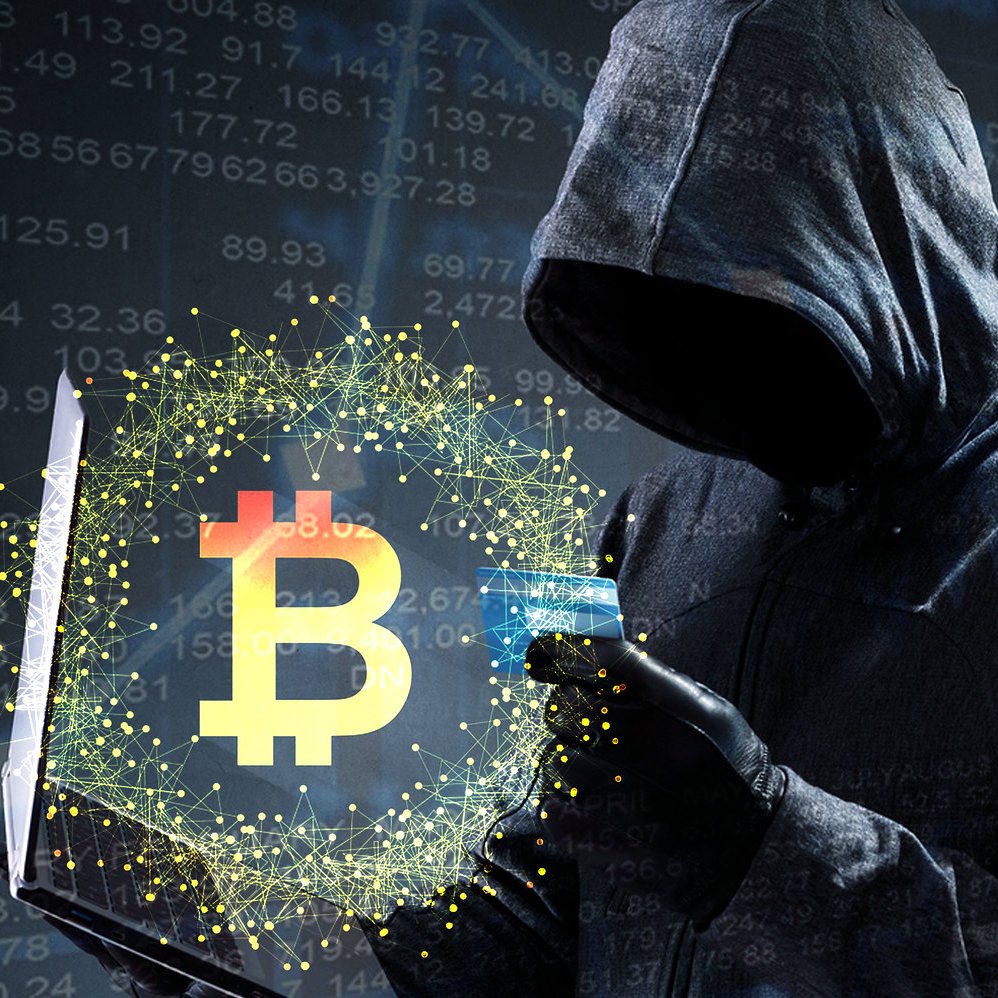 L'image présente une figure mystérieuse, vêtue d'une capuche sombre, qui se tient devant un écran d'ordinateur. Le visage de cette personne est masqué, ce qui ajoute une aura d'intrigue. Dans ses mains, elle tient un ordinateur portable ouvert, avec un symbole de Bitcoin lumineux en surbrillance, entouré d'une aura de particules scintillantes. En arrière-plan, des graphiques financiers et des chiffres évoquent le monde de la cybernétique et de la finance, suggérant des thèmes liés à la cryptomonnaie et au piratage. L'ensemble de l'image dégage une ambiance sombre et technologique.