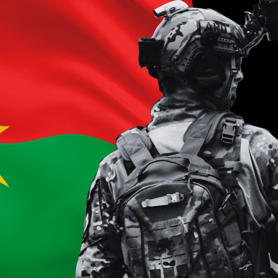 L'image montre un soldat de dos, vêtu d'un uniforme de camouflage, avec un sac à dos. En arrière-plan, se trouve le drapeau du Burkina Faso, qui est composé de bandes horizontales rouges et vertes avec une étoile jaune au centre. Le soldat est positionné de manière à mettre en valeur le drapeau, symbolisant probablement la fierté nationale ou le service militaire.
