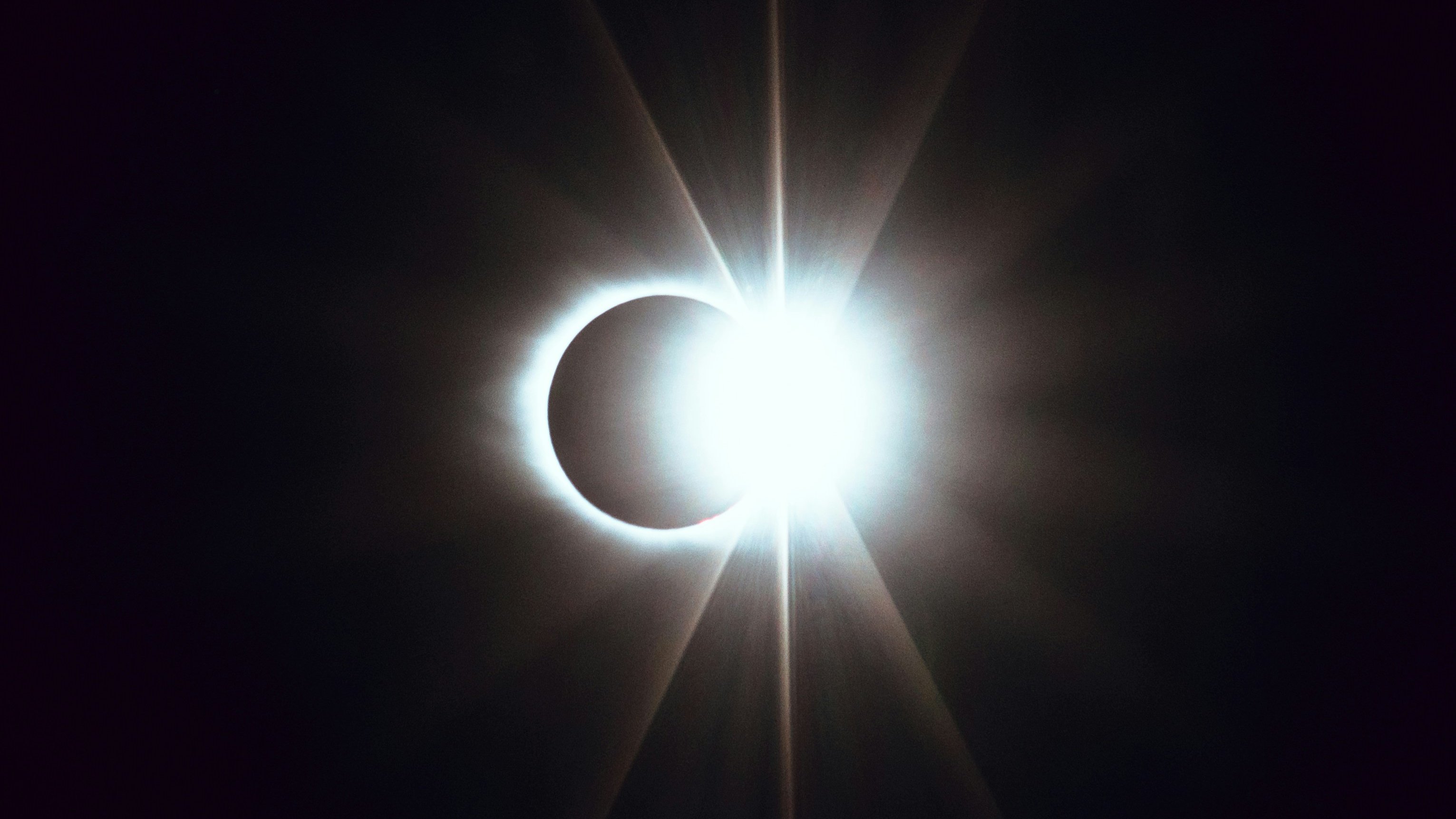 L'image représente un phénomène astronomique spectaculaire : une éclipse solaire. Au centre, un cercle éclatant de lumière intense, représentant le soleil, est partiellement recouvert par la silhouette sombre de la lune. Cette superposition crée un effet visuel époustouflant, où des rays lumineux jaillissent autour du bord de la lune, formant une sorte de couronne brillante. Le contraste entre la lumière vive et l'ombre de la lune évoque une atmosphère immersive, presque mystique, qui attire l'attention et suscite l'émerveillement face à la beauté de l'univers.
