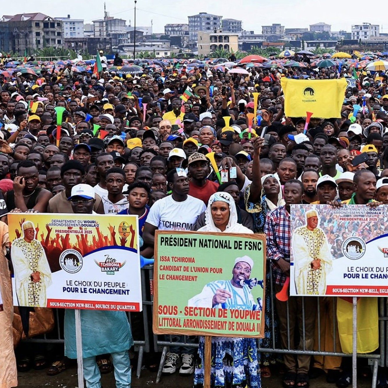L'image montre une grande foule rassemblée pour un événement ou un meeting public. Les gens se tiennent serrés les uns contre les autres, créant une mer de visages et de vêtements colorés. De nombreux participants tiennent des banderoles avec des messages politiques, notamment le slogan "Le choix du peuple pour le changement." On peut également apercevoir des drapeaux flottants, évoquant une atmosphère de mobilisation et d'engagement. L'arrière-plan suggère une ambiance urbaine, avec des bâtiments visibles au loin, tandis que le ciel pourrait être nuageux ou couvert. Ce rassemblement dégage un sentiment d'énergie collective, d'espoir et de désir de changement.