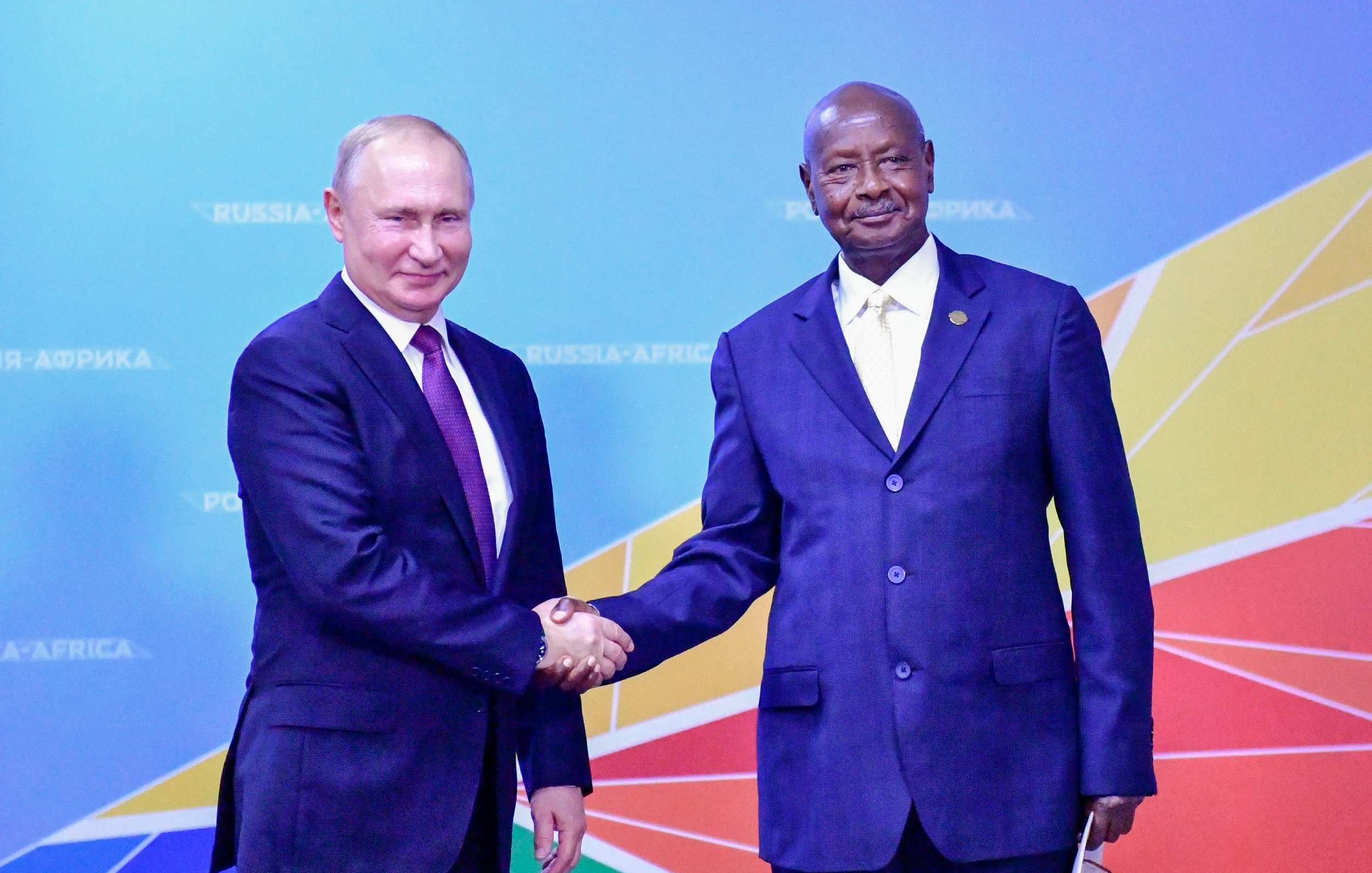 L'image montre deux hommes se serrant la main dans un cadre officiel. À gauche, un homme en costume sombre avec une cravate mauve, qui semble être un dirigeant. À droite, un homme également en costume, mais avec une chemise blanche et une cravate jaune, dégage une certaine dignité. Ils se tiennent devant un fond coloré qui représente une carte stylisée de l'Afrique, avec des couleurs vives comme le rouge, le jaune et le bleu. L'atmosphère est formelle et conviviale, suggérant une rencontre ou un accord important entre les deux leaders.