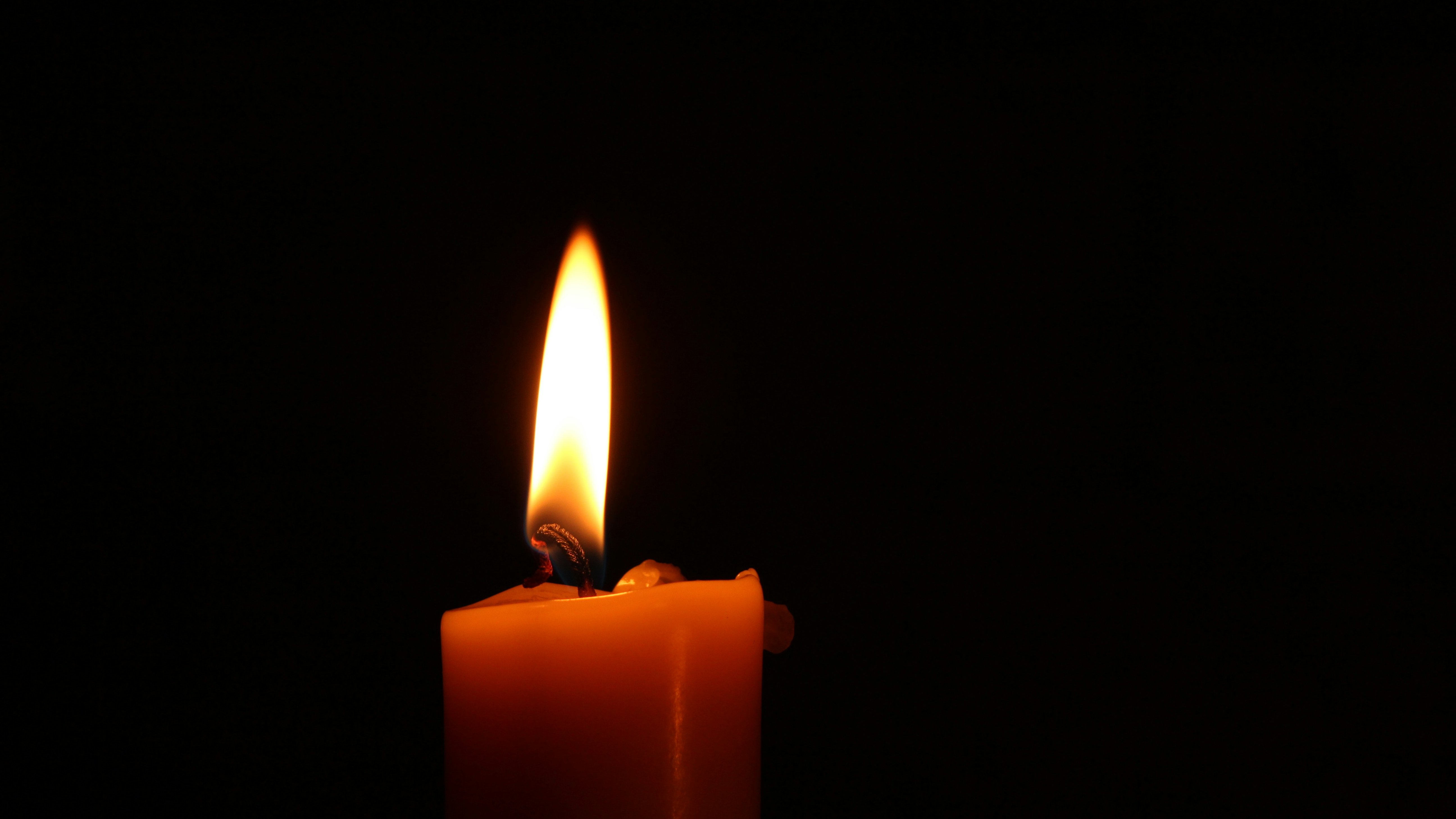 L'image présente une bougie allumée dans un environnement sombre. La flamme, vive et dansante, émet une lumière chaleureuse et douce, créant une atmosphère calme et apaisante. La surface de la bougie est lisse et de couleur jaune ou orange, et la mèche, légèrement recourbée, est en train de se consumer doucement. La lumière de la flamme projette des ombres délicates autour, accentuant l'obscurité environnante. Cette scène évoque une sensation de sérénité et de chaleur, typique d'un moment de méditation ou de recueillement.