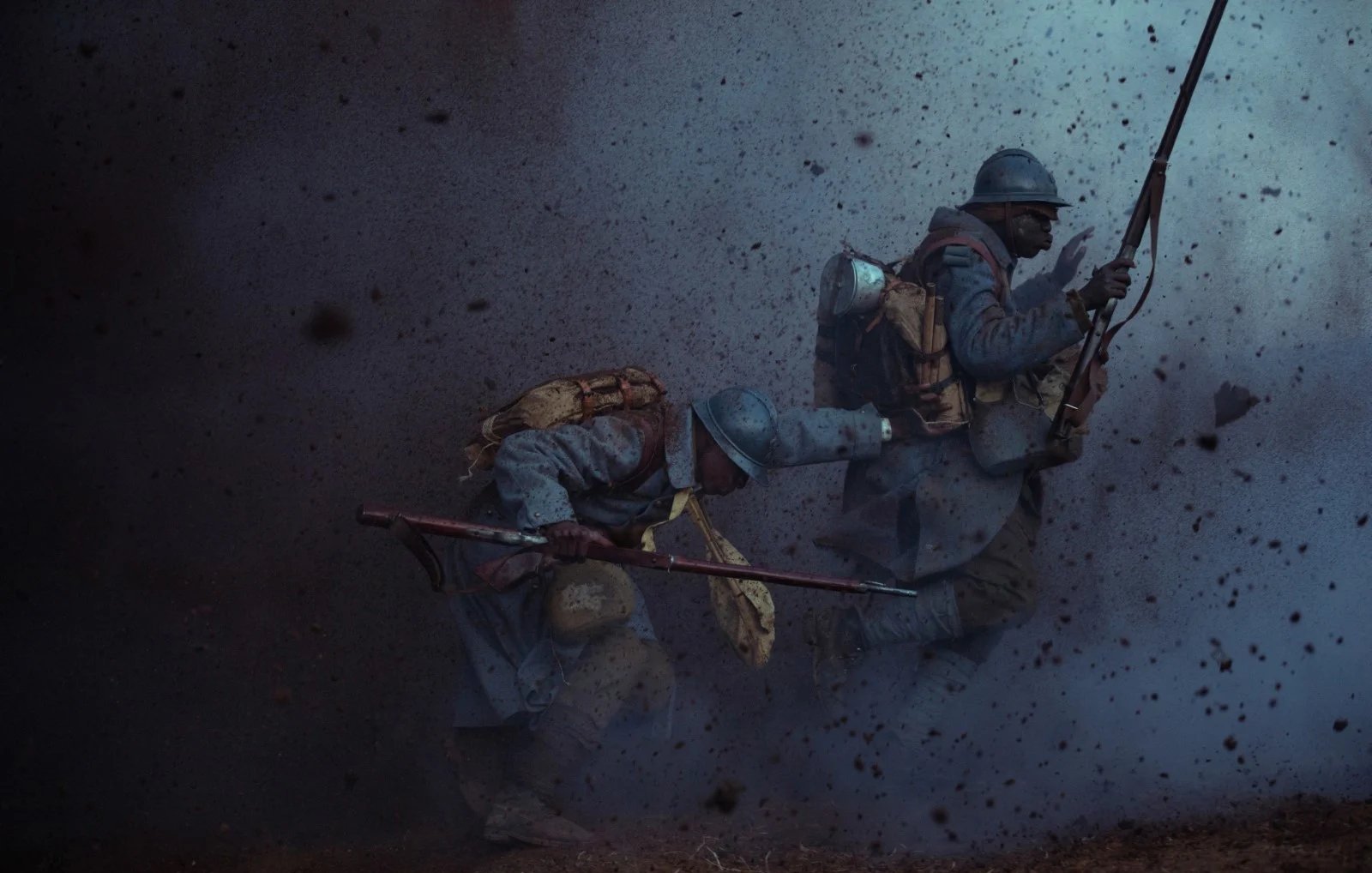 L'image dépeint une scène de guerre intense. Deux soldats, habillés de uniformes bleu ciel typiques de la Première Guerre mondiale, avancent avec détermination à travers un paysage chaotique. On ressent une ambiance de tension et de danger, accentuée par des éclats de poussière et de débris qui volent autour d'eux, comme si une explosion venait de se produire. Les soldats portent des sacs à dos lourds et sont armés de fusils, montrant leur préparation au combat. Leur position angulaire suggère un mouvement rapide, soulignant le courage et l'adrénaline de la situation. L'éclairage est sombre, créant une atmosphère pesante, presque apocalyptique.