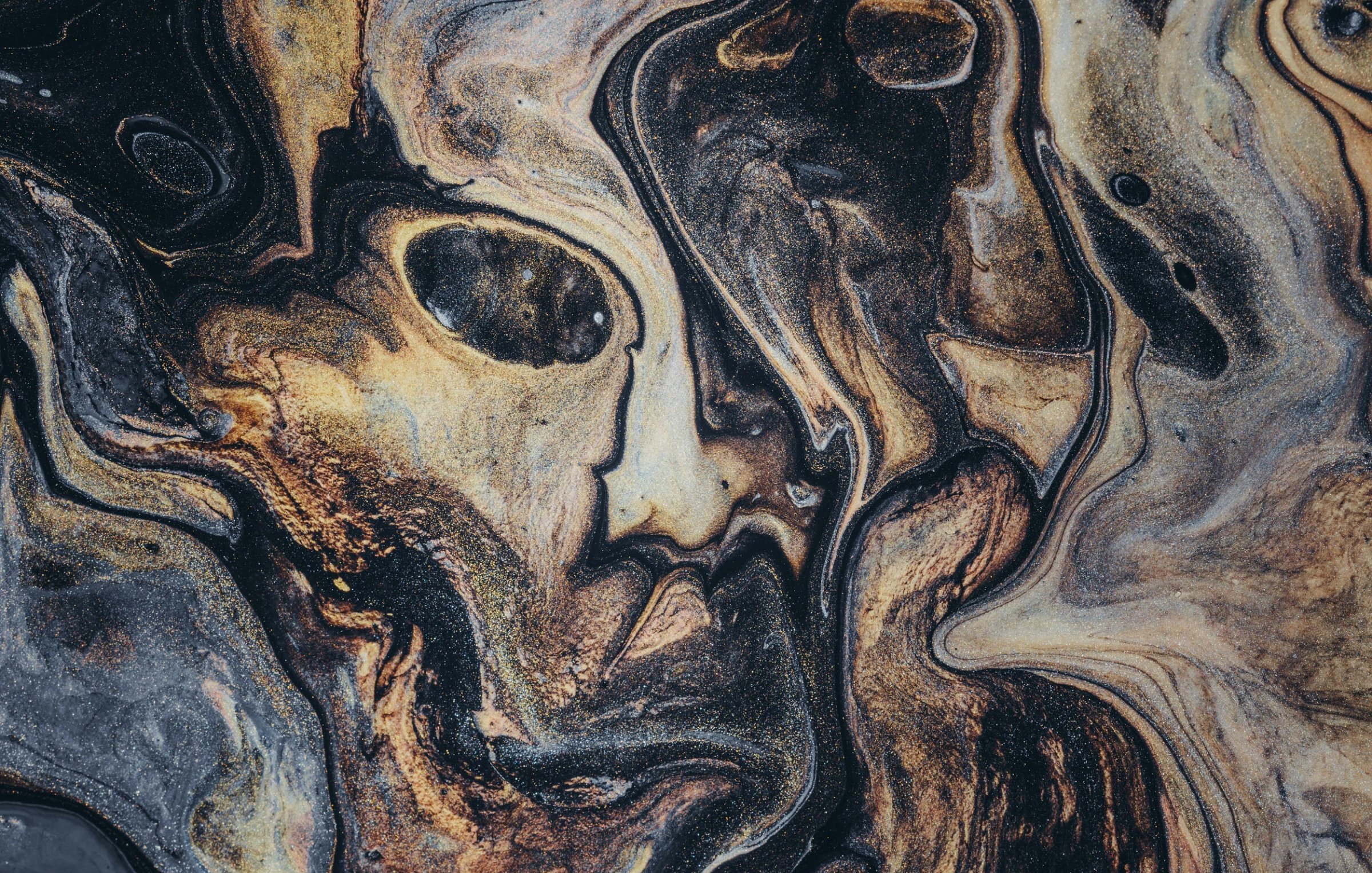 L'image présente un motif abstrait et fluide, où les couleurs noir, or et brun s'entrelacent de manière sinueuse. On peut presque percevoir des formes humaines dans ce mélange, évoquant des visages ou des silhouettes cachés dans la texture. Les lignes sont tourbillonnantes et créent une dynamique qui capte l'attention, semblant vibrer comme si elles prenaient vie. L'ensemble dégage une atmosphère mystérieuse et intrigante, invitant à l'exploration des détails et des effets de couleur.