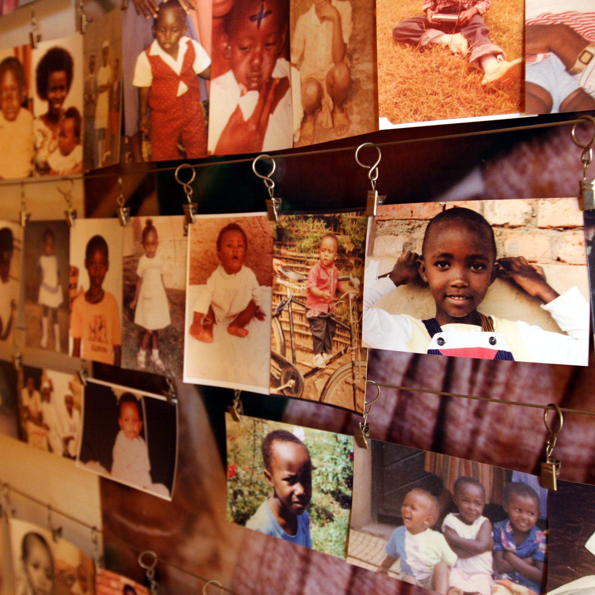L'image montre un grand mur couvert de nombreuses photos accrochées avec des pinces. Ces images, en couleur et en noir et blanc, illustrent des enfants de différents âges, principalement des jeunes enfants. Les visages des enfants expriment souvent des sourires ou des poses amusantes. Les photos sont en désordre, ce qui crée une scène vivante et nostalgique, évoquant des souvenirs d'enfance. Le fond est neutre, permettant aux photos de se démarquer et de raconter des histoires individuelles de joie et d'innocence.