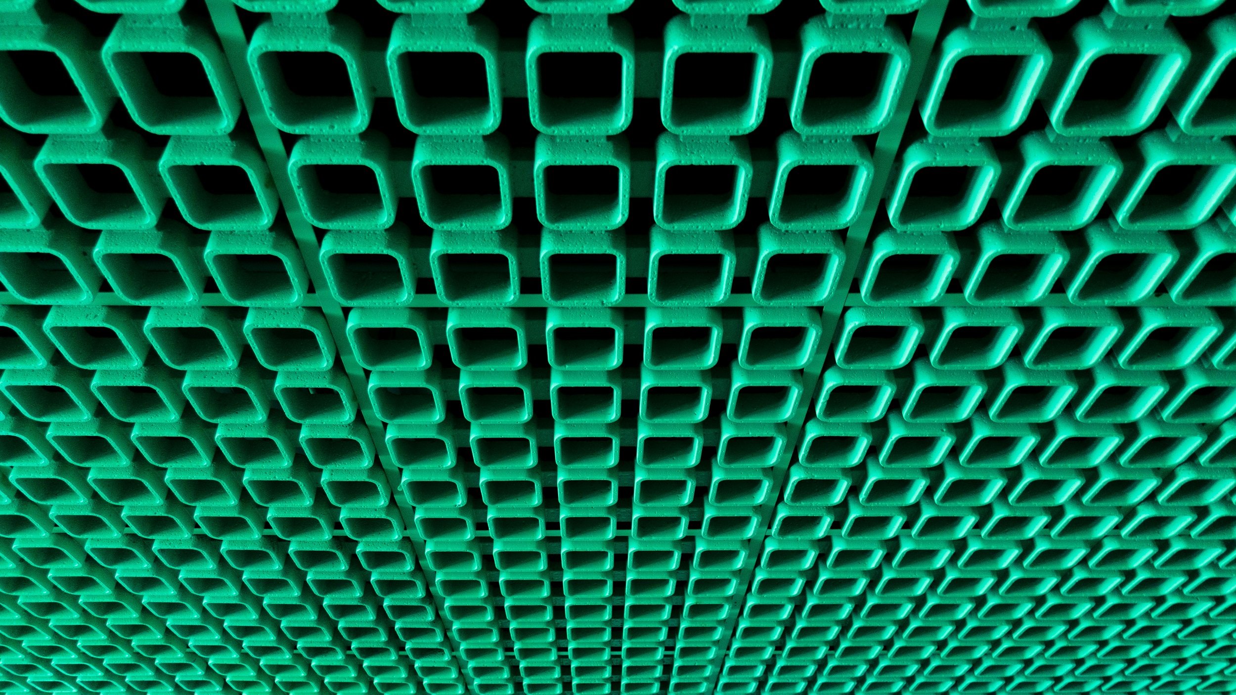L'image montre un motif répétitif de carrés de couleur verte. Ces carrés sont disposés de manière régulière et forment une sorte de grille ou de treillis. La texture semble lisse, et les angles des carrés sont bien définis. L'ensemble crée une impression de profondeur et de répétition, avec une lumière qui pourrait accentuer les ombres des différents éléments. Cette composition évoque une sensation de structure et d'ordre.
