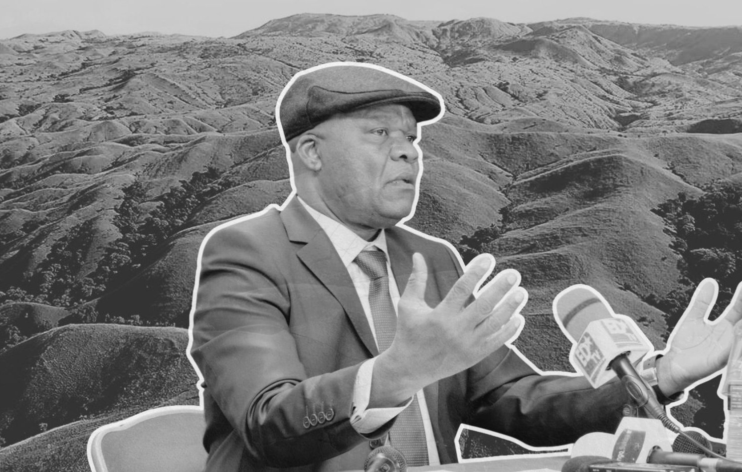 The image features a man in a suit and a cap, gesturing while speaking at a press conference or similar setting. He appears to be in front of a landscape of rolling hills or mountains, which are shown in a monochrome style to highlight the subject. The background scenery emphasizes the natural environment, contrasting with the formal attire of the man, who seems to be making an important point. The overall composition combines elements of nature and a formal discussion.