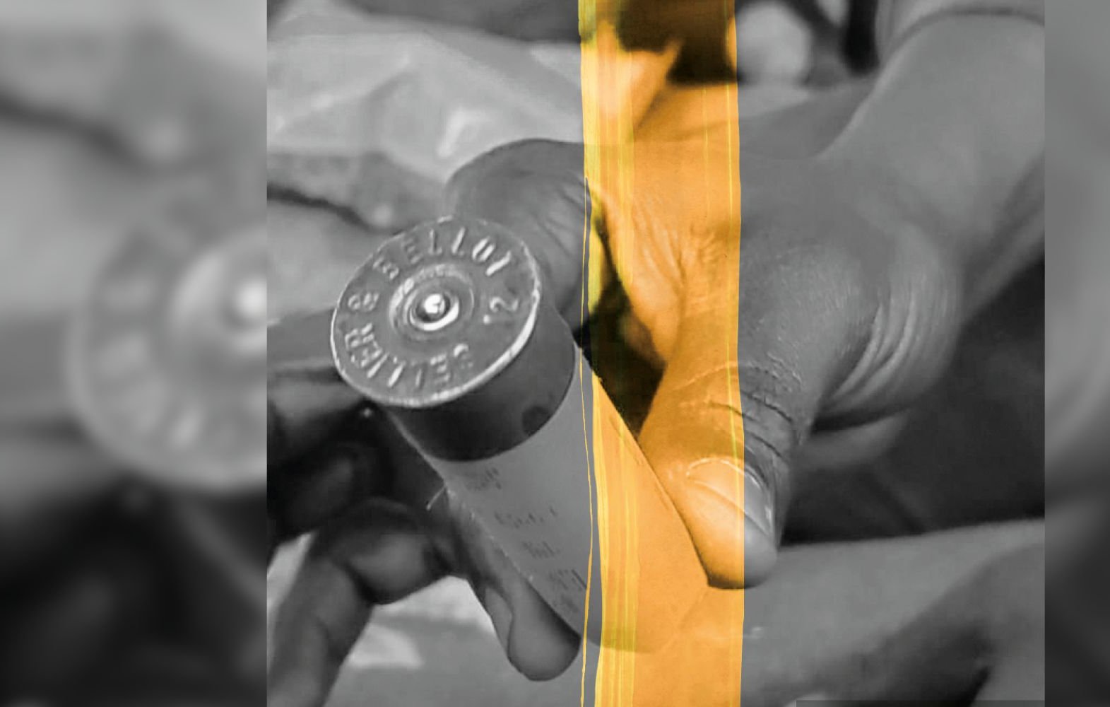 L'image montre deux mains tenant une cartouche de balle. La cartouche est de taille cylindrique et présente des inscriptions sur le côté, ainsi qu'un fond plat. Les mains sont légèrement enroulées autour de la cartouche, montrant un geste de manipulation. Le fond est flou, mettant en avant l'objet au centre de l'image. Les couleurs semblent être réduites à des nuances de noir et blanc, accentuant le contraste entre les mains et la cartouche. L'atmosphère générale est sérieuse, indiquant peut-être une situation de travail ou de préparation.