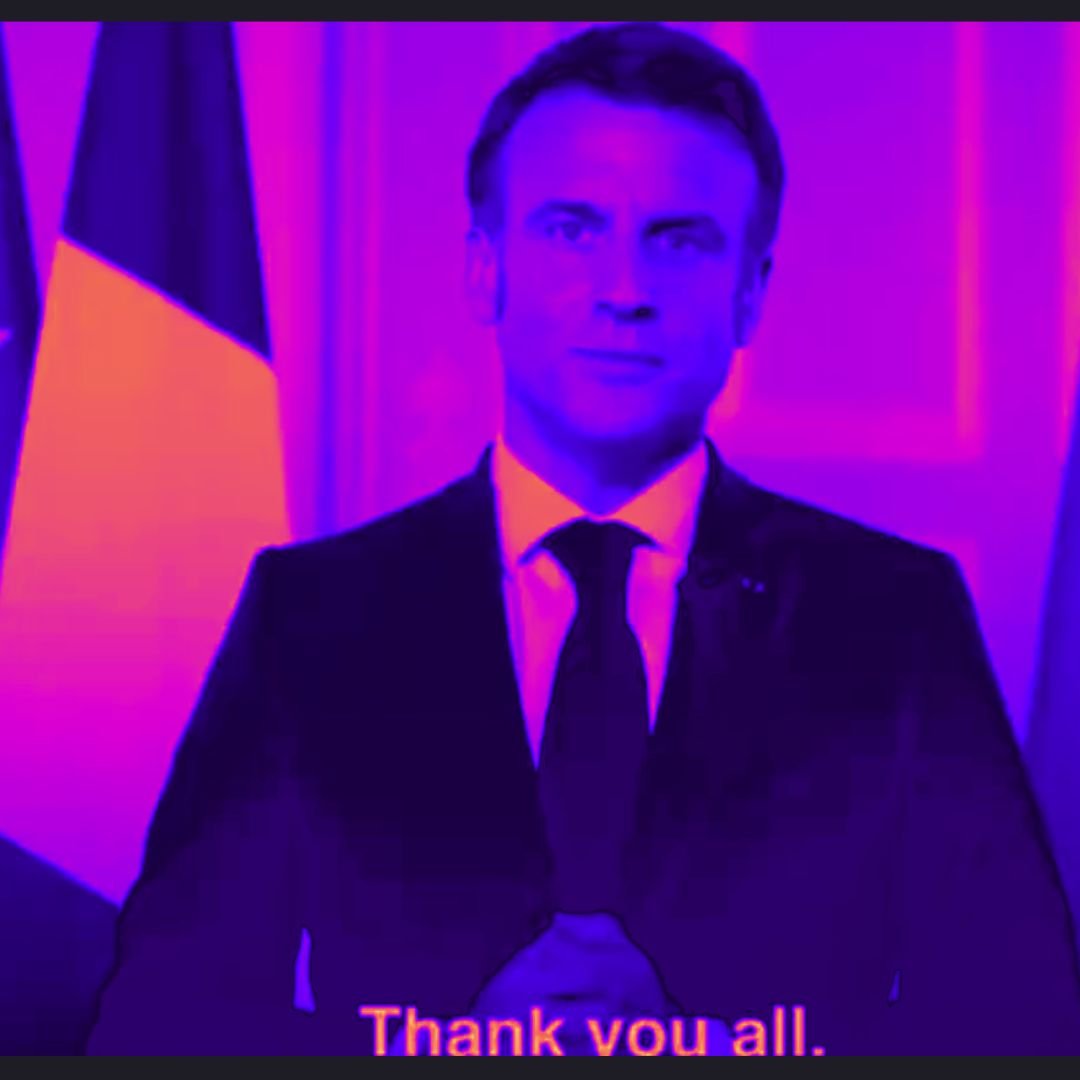 L'image montre un homme en costume sombre, debout devant un arrière-plan aux tons violets et roses. Il a une expression sérieuse et est placé entre deux drapeaux : un drapeau tricolore français à gauche et un autre qui pourrait représenter l'Argentine à droite. Ses mains sont jointes devant lui, comme s'il allait s'exprimer. En bas de l'image, on peut lire un texte en anglais qui dit "Thank you all", indiquant qu'il s'adresse à un auditoire. L'ensemble de la scène dégage une atmosphère formelle et solennelle.