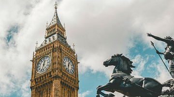 L'image présente une vue majestueuse de la célèbre horloge de Big Ben à Londres. Le bâtiment, en pierre, se distingue par sa hauteur impressionnante et ses ornements dorés. Les deux grands cadrans d'horloge sont visibles, indiquant l'heure avec des chiffres romains. En bas à droite, une statue en bronze d'un cavalier sur un cheval ajoute une touche historique et dynamique à la scène. Le ciel est partiellement nuageux, ce qui crée un contraste intéressant avec l'architecture dorée et les détails du monument. L'ensemble dégage une atmosphère à la fois emblématique et intemporelle.