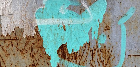 L'image présente une surface en métal, probablement rouillée, avec des marques et des textures variées. On y voit une tache de couleur turquoise qui semble avoir été projetée. Cette tache a une forme fluide et irrégulière, évoquant une sorte de mouvement ou de dynamisme. À proximité, on peut distinguer des traces brunes, résultant de la rouille, qui ajoutent un contraste marqué à la couleur vive. Le fond est texturé, avec des stries et des imperfections, suggérant l'âge et l'usure du matériau. L'ensemble crée une atmosphère à la fois urbaine et artistique.